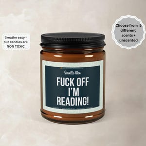 May include: A brown glass jar candle with a black lid. The label reads "Smells like FUCK OFF I'M READING!". Additional text states the candles are non-toxic and available in 5 scents. The candle is hand-poured in the USA.