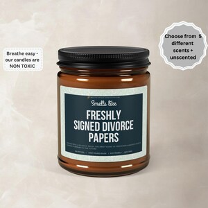 May include: A brown glass jar candle with a black lid. The label reads "Smells like Freshly Signed Divorce Papers." Additional text includes "Breathe easy - our candles are NON TOXIC" and "Choose from 5 different scents + unscented."