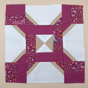 May include: A square quilt block featuring a geometric design. The block incorporates white, burgundy, and tan fabrics. Some sections have a floral pattern with berries and leaves. The block is likely for a quilt or other textile project.