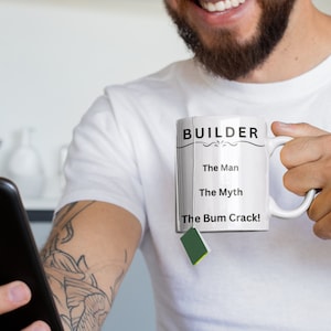Puede incluir: Taza de cer&aacute;mica blanca con texto negro que dice "BUILDER The Man The Myth The Bum Crack!" Una persona sostiene la taza con una bolsita de t&eacute; colgando del borde.