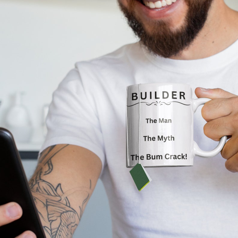 Puede incluir: Taza de cer&aacute;mica blanca con texto negro que dice "BUILDER The Man The Myth The Bum Crack!" Una persona sostiene la taza con una bolsita de t&eacute; colgando del borde.