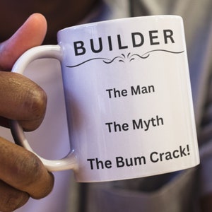 Puede incluir: Taza de cer&aacute;mica blanca con asa negra. La taza tiene la palabra "BUILDER" impresa en negro, seguida del texto "The Man", "The Myth" y "The Bum Crack!" en negro.