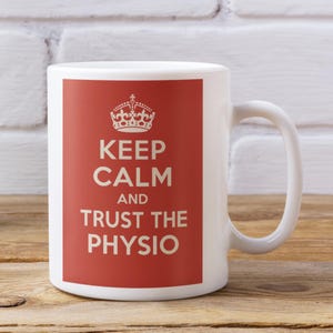 May include: White ceramic mug with a red panel displaying the text "KEEP CALM AND TRUST THE PHYSIO" in white, and a crown graphic. The mug has a curved handle.