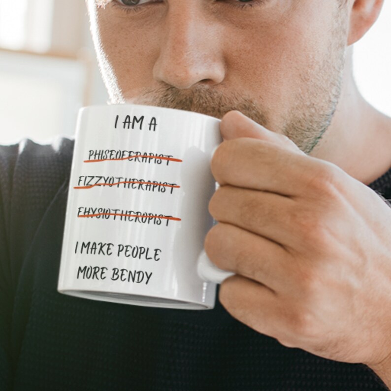 A white 11oz ceramic coffee mug for Physiotherapists with the funny caption "I am a Physiotherapist" But it is crossed out three times miss spelt. The caption then says at the bottom "I make people more bendy"