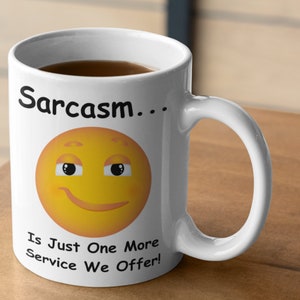 Pode incluir: Caneca de café de cerâmica branca com um rosto sorridente amarelo e o texto "Sarcasmo... É apenas mais um serviço que oferecemos!"