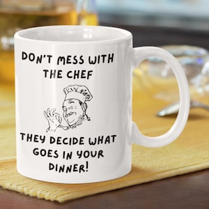 Pode incluir: Caneca de cerâmica branca com uma ilustração preta de um chef e o texto "Não mexa com o chef. Ele decide o que vai no seu jantar!"