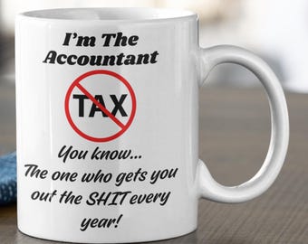 Puede incluir: Taza de café de cerámica blanca con un gráfico negro y rojo que dice "I'm The Accountant" con un círculo rojo y una línea diagonal a través de la palabra "TAX". El texto debajo del gráfico dice "You know... The one who gets you out the SHIT every year!"