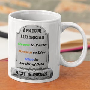 May include: White ceramic mug with a humorous design. The mug features a tombstone graphic with the words "AMATEUR ELECTRICIAN" and wiring instructions. The bottom of the tombstone reads "REST IN PIECES".