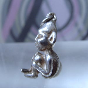 Peut inclure: Un charme en argent en forme de petite figurine assise portant un chapeau pointu. La figurine a un visage détaillé et porte un vêtement simple.