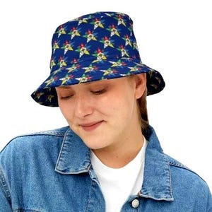 Puede incluir: Un gorro de pescador azul con un patrón repetido de estrellas amarillas, blancas y rojas. El gorro lo lleva una persona con una chaqueta vaquera.