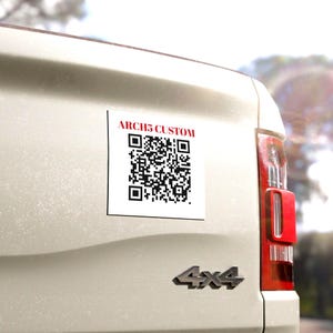 Może przedstawiać: Biała kwadratowa naklejka z czarnym kodem QR i czerwonym tekstem "ARCH5 CUSTOM" jest przymocowana do tyłu jasnego pojazdu. Naklejka umieszczona jest w pobliżu tylnego światła.