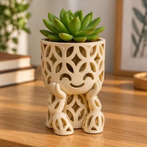 May include: A cream-coloured planter shaped like a seated figure with hands resting on its cheeks. The planter features an intricate, open-work geometric pattern throughout its body and holds a vibrant green succulent plant on its top surface.