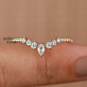 May include: A delicate gold ring with a pear-shaped diamond in the center and smaller round diamonds on either side, forming a V-shape.