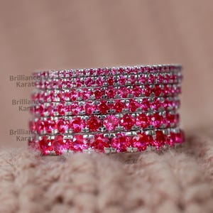 May include: Stack of thin silver rings with pink rhinestones. Each ring is set with a row of small pink stones.