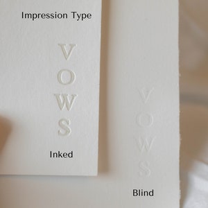 May include: Close-up of two white cards with the word "VOWS" embossed in different ways. The card on the left has the word "VOWS" embossed in ink, while the card on the right has the word "VOWS" embossed in blind. The card on the left is labeled "Inked" and the card on the right is labeled "Blind".