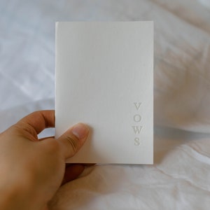 May include: A white booklet with the word "VOWS" embossed on the front cover.
