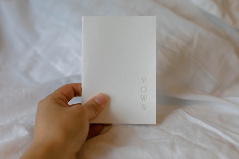 May include: A white booklet with the word "VOWS" embossed on the front cover.