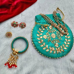 May include: A teal fabric pouch with gold embroidery and pearl accents. The pouch is decorated with a floral design and has a drawstring closure. The pouch is accompanied by a matching bangle with a tassel, a pair of earrings, and a necklace.