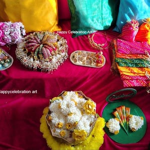 Könnte beinhalten: Ein roter Samttisch mit verschiedenen Gegenständen für eine traditionelle indische Hochzeitszeremonie.  Die Gegenstände umfassen ein Tablett mit Süßigkeiten, einen dekorativen Teller mit einer Blumenarrangements, ein Tablett mit Schmuck und einen Stapel bunter Stoffbeutel. Der Text "Happy Celebration Art" ist im Bild sichtbar.