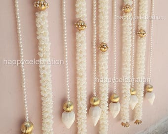 May include: Cream-colored floral garlands with pearl strands and gold accents. The garlands are hanging against a light pink wall. The text "happycelebration" is visible on the image.