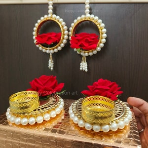 Puede incluir: Dos decoraciones colgantes doradas con rosas rojas y detalles de perlas blancas. Dos candelabros dorados con rosas rojas y detalles de perlas blancas. El texto "Happy Celebration art" es visible en la imagen.