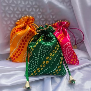 Puede incluir: Tres pequeñas bolsas de cordón hechas de tela con un diseño estampado de colores. Las bolsas son naranja, verde y rosa con detalles blancos y amarillos. Las bolsas tienen ribetes dorados y borlas.