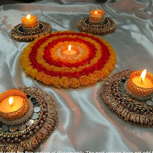 May include: Four golden candle holders with lit tea lights are arranged on a white satin surface. A circular floral arrangement with yellow and red roses surrounds a fifth candle holder.