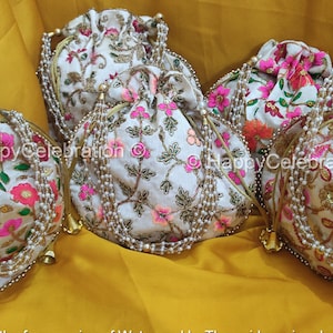 May include: Four white drawstring bags with floral embroidery and pearl embellishments. The bags have gold handles and are arranged on a yellow surface.