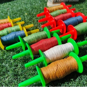 May include: A collection of colorful spools of string, each with a plastic handle, are arranged on a green grassy surface. The spools are in various colors, including red, green, blue, yellow, and brown.
