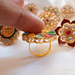 May include: A set of colorful, gold-tone, decorative rings with various designs. The rings feature a variety of gemstones, including red, green, blue, and yellow. The rings are set on a white background.