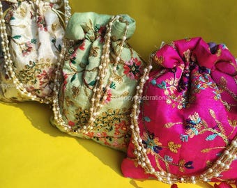 May include: Three embroidered drawstring bags with pearl chains. The bags are in shades of cream, green, and pink with floral patterns. The bags are on a yellow surface.