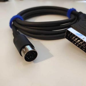 Peut inclure: Un câble vidéo noir Atari ST avec un connecteur SCART 15 broches à une extrémité et un connecteur DIN 9 broches à l'autre extrémité.
