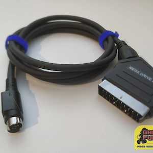 Puede incluir: Un cable AV negro Sega Genesis 2 con un conector RCA negro en un extremo y un conector SCART negro en el otro extremo. El conector SCART tiene el texto "MEGA DRIVE 2" impreso en él.