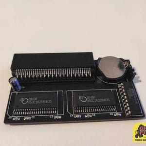 Könnte beinhalten: Nahaufnahme einer schwarzen Platine mit zwei Chips, die mit "0103F V53C16258HK35" und "9745F V53C16258HK35" beschriftet sind. Die Platine hat eine Reihe von Pins und eine runde silberne Batterie.