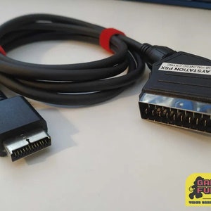 Könnte beinhalten: Ein schwarzes PlayStation PSX RGB PAL/NTSC CSYNC-Kabel mit einem SCART-Stecker an einem Ende und einem schwarzen Stecker am anderen Ende.