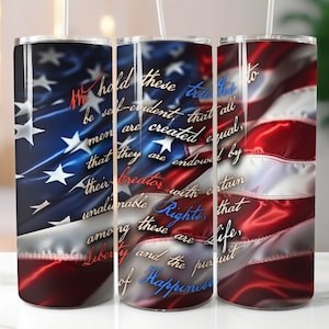May include: Three stainless steel tumblers with a patriotic design featuring the American flag. The flag's red and white stripes and blue field with stars are visible. Text from the Declaration of Independence is overlaid on the flag.