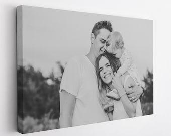 May include: A black and white photograph of a family of three. A man and woman are holding a young child. The child is kissing the man on the cheek. The family are smiling and appear to be happy.