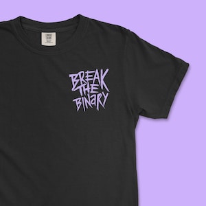 Może przedstawiać: Czarny t-shirt z napisem "BREAK THE BINARY" w lawendowym kolorze. Tekst jest w stylizowanej czcionce. Koszulka ma okrągły dekolt i krótkie rękawy. Mała metka jest widoczna po lewej stronie u góry.