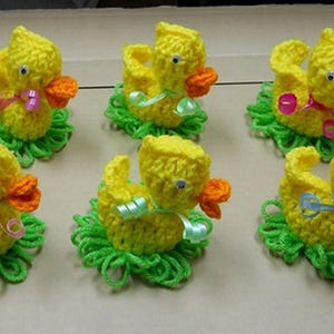 Puede incluir: Seis figuritas de pato amarillo de crochet con bases de hierba verde y detalles de cinta de colores.