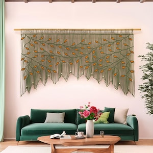 Extra large olive green macrame wall hanging with terracotta leaf vines hanging over a green sofa