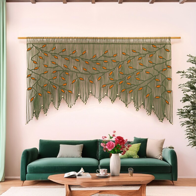 Extra large olive green macrame wall hanging with terracotta leaf vines hanging over a green sofa