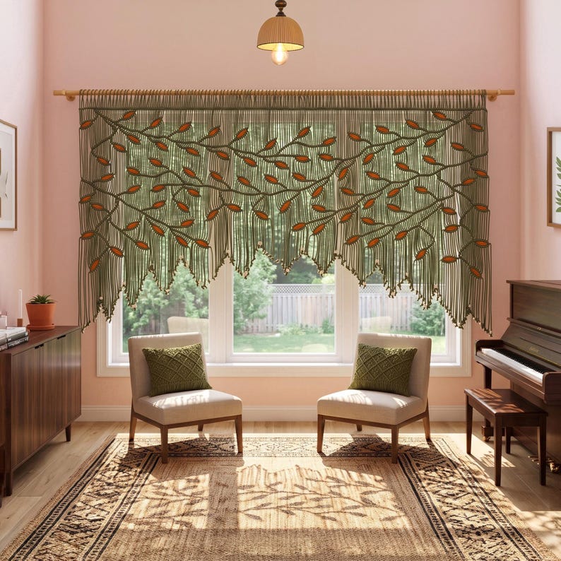 May include: A macrame window valance featuring a sage green knotted cord design with integrated orange leaf-shaped accents. The piece hangs from a wooden rod, displaying a cascading vine pattern that spans the width of the window frame.