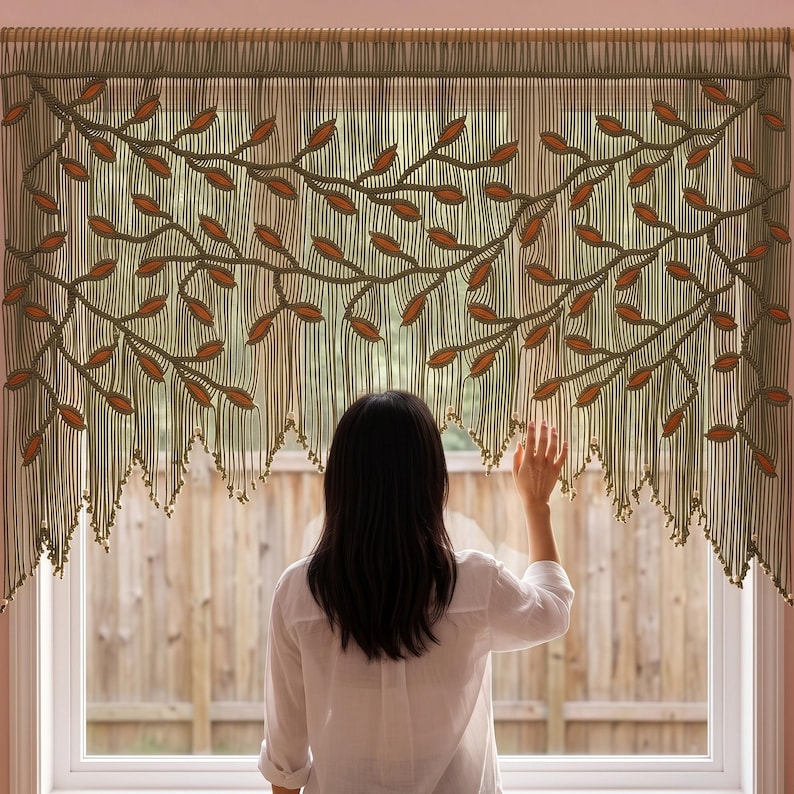May include: A macrame window valance featuring a repeating vine pattern in olive green cord with integrated burnt orange leaf accents. The design includes a series of vertical hanging strands that terminate in a pointed, uneven fringe edge.