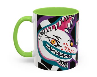 Peut inclure: Mug en céramique blanche avec une anse et un intérieur verts. La tasse présente une illustration de dessin animé d'une créature avec des dents pointues, des taches rouges et des yeux jaunes. Le design comprend des accents noirs, roses et violets.