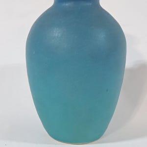 May include: A small, round, light blue ceramic vase with a smooth, matte finish.