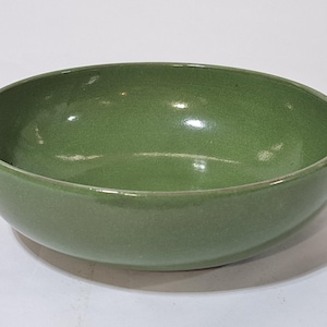 May include: A green ceramic bowl with a smooth, glossy finish. The bowl has a rounded shape and a wide opening. The color is a muted, earthy green. The bowl is likely used for serving food or as a decorative item.
