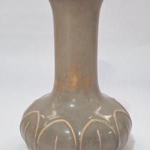 May include: A gray ceramic vase with a bulbous base and a slender neck. The base features a repeating pattern of curved lines in a lighter shade, and the neck flares slightly at the top. The vase has a smooth, matte finish.