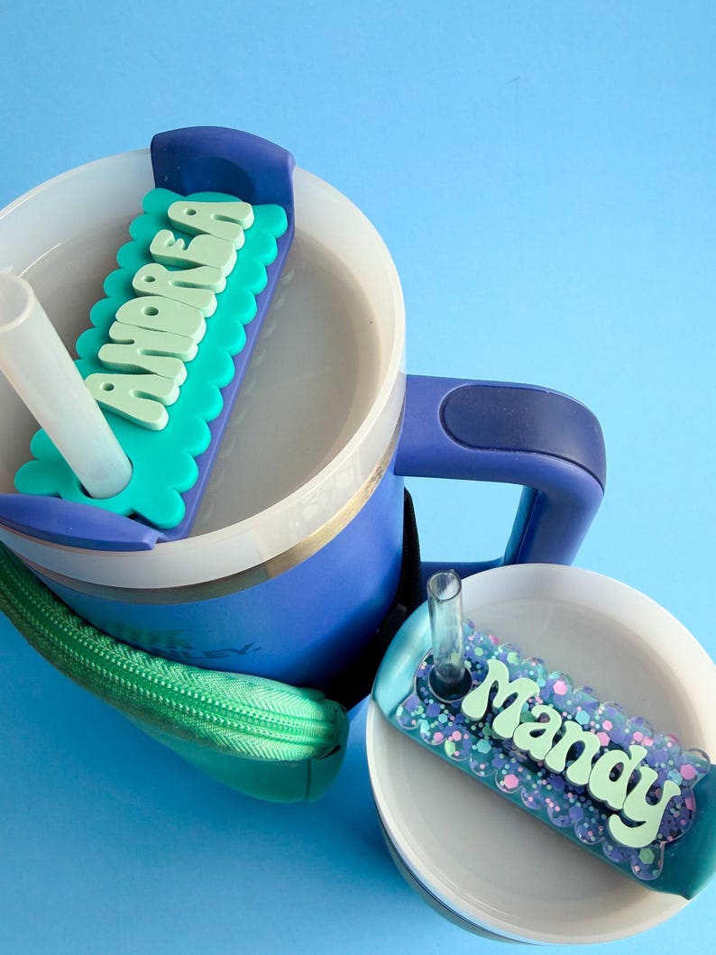 A blue and white sippy cup with a personalized name tag attached to it, sitting on a blue surface.