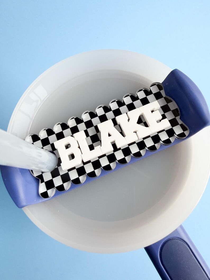 A white bowl with the name "BLAKE" written on it in large letters, placed on a blue surface.
