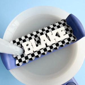 A white bowl with the name "BLAKE" written on it in large letters, placed on a blue surface.